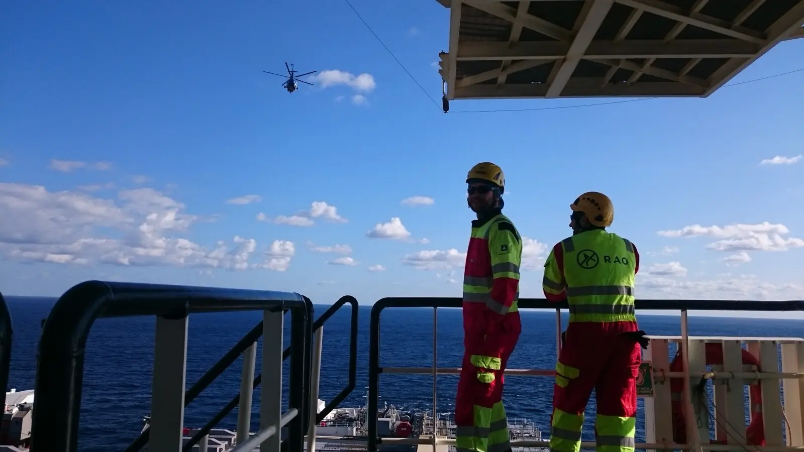 Deux techniciens sur le pont d'une plateforme, un hélicoptère en arrière-plan