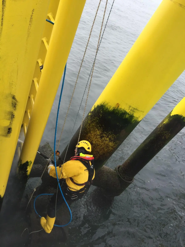 Technicien cordiste sur une fondation jaune, juste au-dessus de l’eau