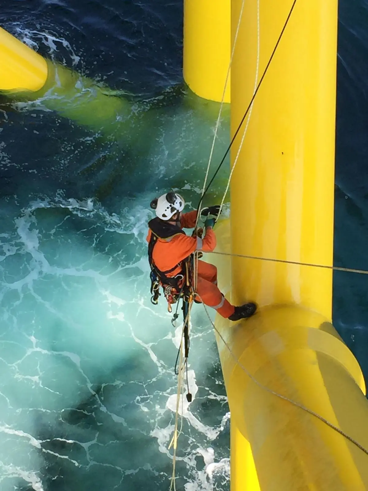 Technicien cordiste au niveau d'un tube jaune au-dessus d'une mer agitée