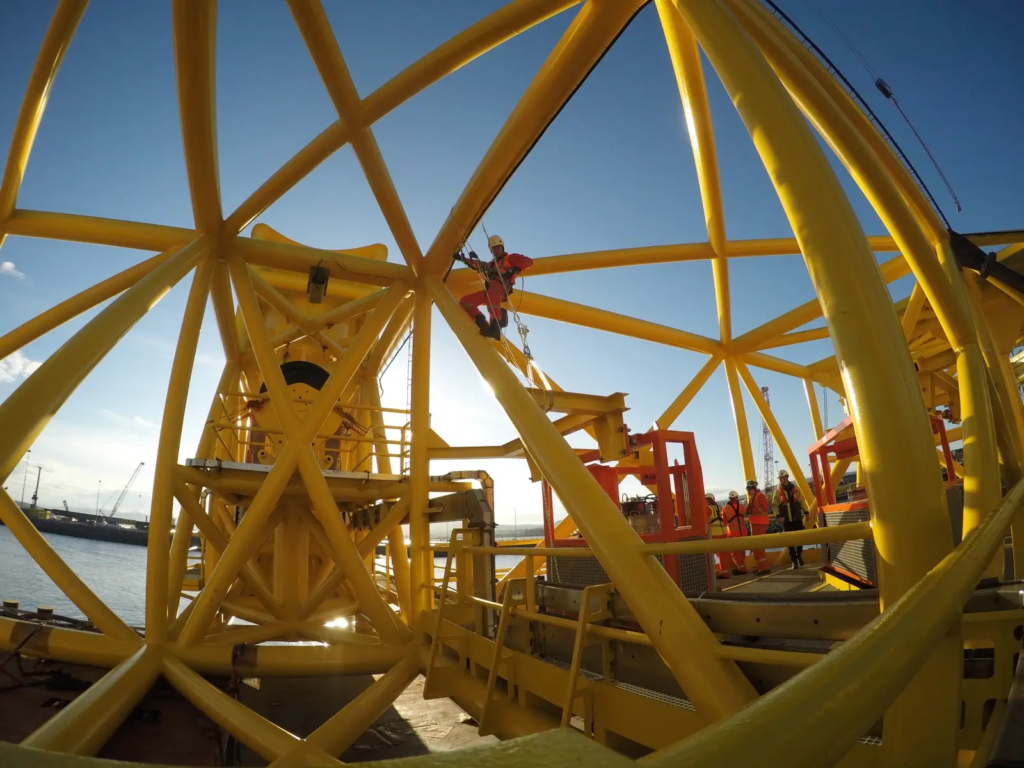 Technicien cordiste sur la structure en treillis jaune d’une fondation offshore