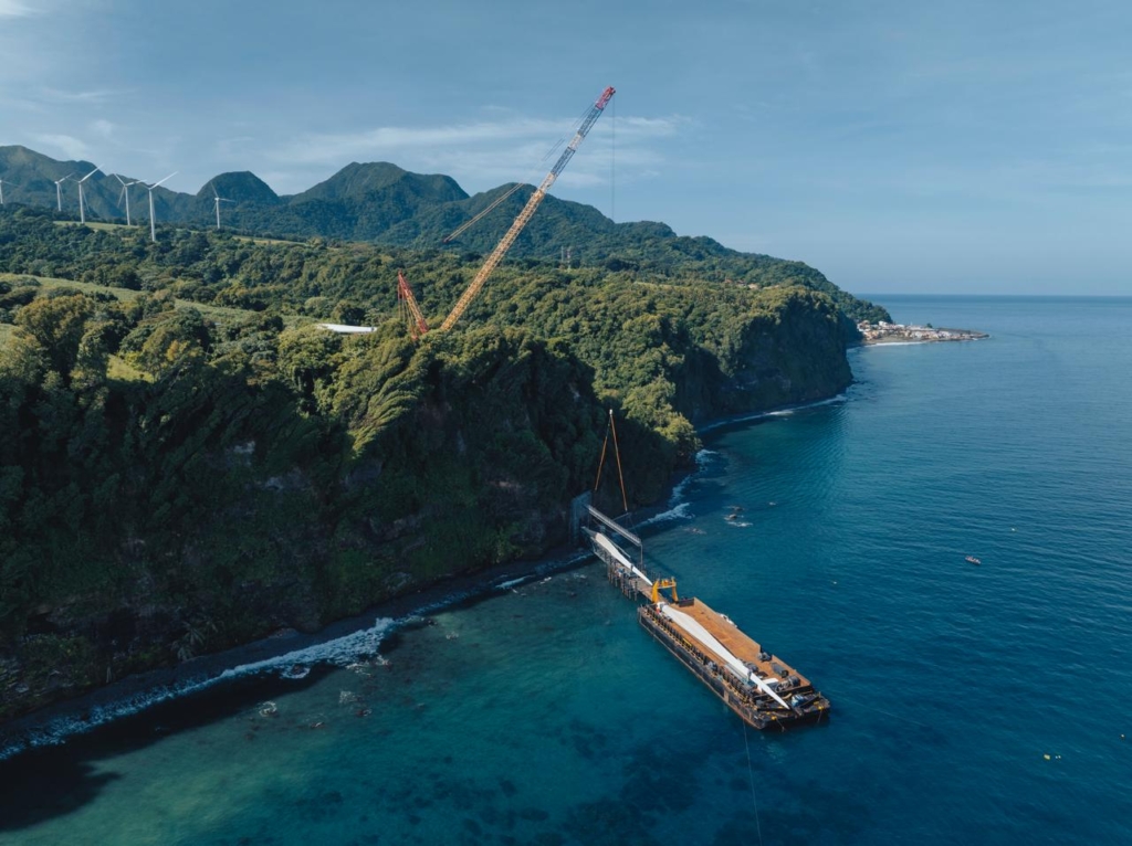 Drone view: a barge by a rocky cliff, a crane on the slope and the sea