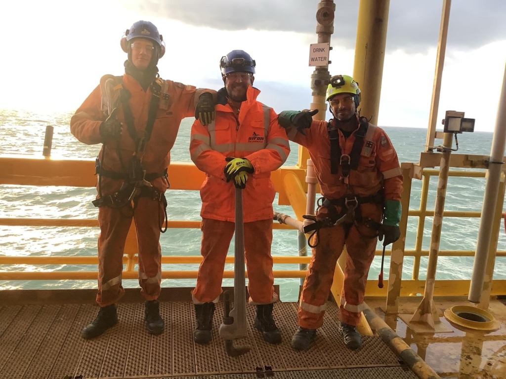 Trzech pracowników w pomarańczowych kombinezonach i kaskach na platformie offshore
