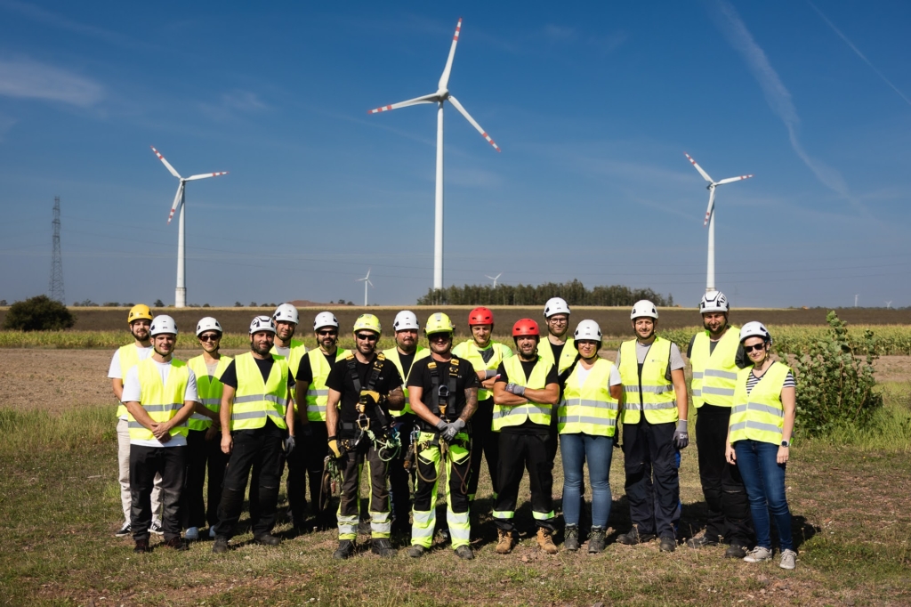 Grupa uczestników Safety Day w kamizelkach odblaskowych i kaskach przed turbinami wiatrowymi