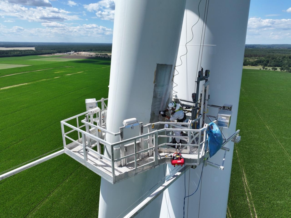 Platforma serwisowa przy łopacie turbiny wiatrowej na tle zielonych pól